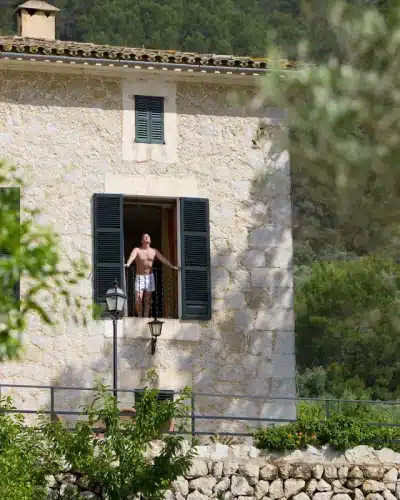 Homme ouvrant les volets de sa maison avec une façade en pierre
